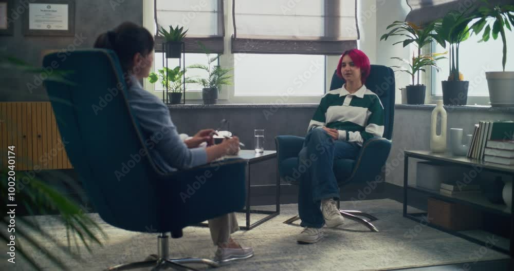 Sticker In psychotherapy room, teenage girl talks to her therapist, shares positive emotions during counseling session. Back view of female psychologist sitting in chair, providing therapy for to teenager.