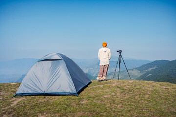 An adventurer stands beside a camping tent, looking at the mountain view &mdash; a perfect moment of travel and adventure.