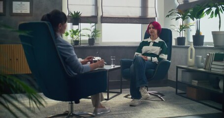 In psychotherapy room, teenage girl talks to her therapist, shares positive emotions during counseling session. Back view of female psychologist sitting in chair, providing therapy for to teenager.