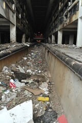 A narrow, debris-filled corridor in a damaged building, with a glimpse of the upper levels.