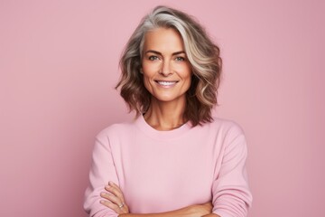 Happy mature woman with folded arms looking at camera and smiling while standing against pink background