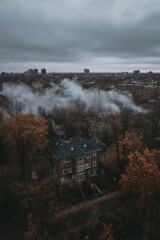A moody aerial view of a cityscape with autumn trees and smoke rising from buildings.