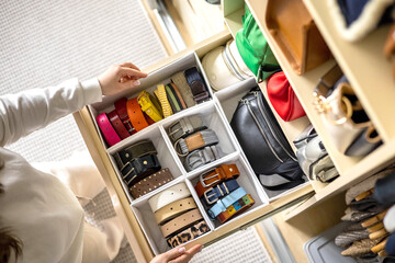 A young beautiful woman puts a convenient order in storing belts in her home wardrobe. 