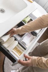 Top view of woman hands neatly organizing bathroom amenities and toiletries in drawer in bathroom.