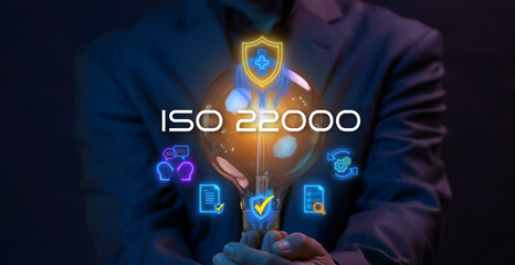 ISO 22000. International Organization for Standardization sign and symbol. Food safety standard. Businessman holding lightbulb to show glowing neon line of ISO 22000 banner icons on virtual screen.