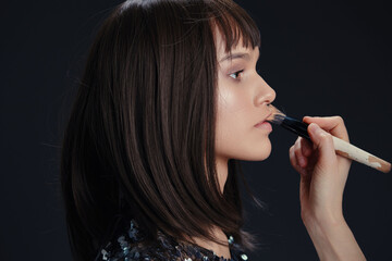 Obraz premium A woman with long brown hair brushes her hair using a brush against a black background, highlighting hair care and grooming