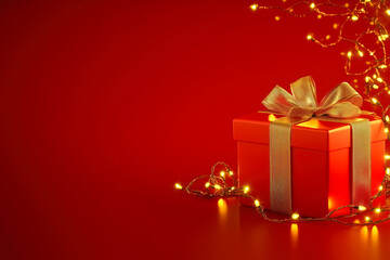 Obraz premium Gift box in red adorned with golden ribbon and fairy lights