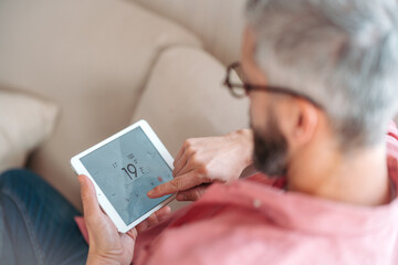 Man using smart thermostat, adjusting, lowering heating temperature at home. Concept of...