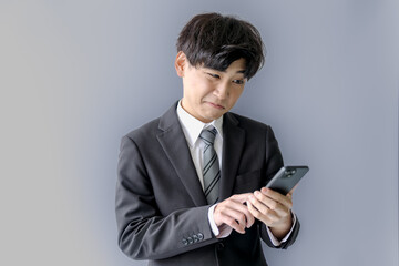 凄い表情でスマホを見る若いスーツ男性