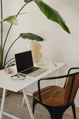 Modern Workspace with Laptop, Glasses, and Lamp on White Desk Amidst Lush Greenery. Home Office...