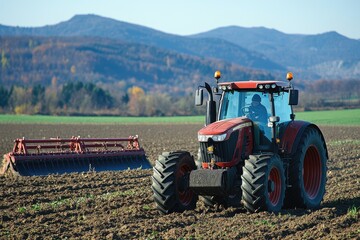 Obraz premium Red tractor working in field. A red tractor is plowing a field with a red plow attachment.