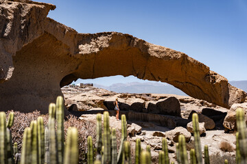 A traveler standing beneath a natural rock arch in a desert landscape