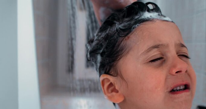 Child wincing as water rinses shampoo from hair in ultra slow-motion, captured with high speed camera, emotional expression, intimate shower moment, gentle care