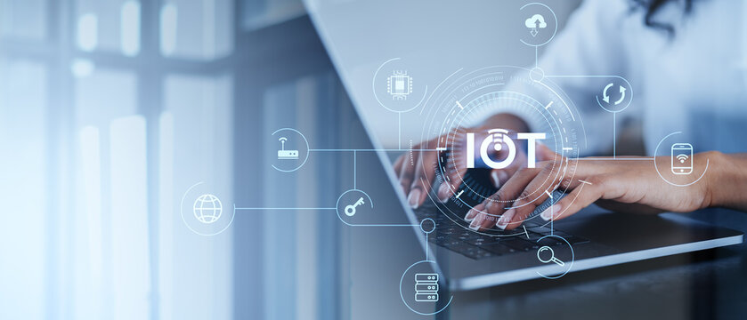Hands typing on a laptop with various IoT hologram icons overlay. The background is blurred, emphasizing the concept of internet connectivity and technology