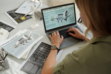 High angle of hands of young businesswoman typing on keyboard of laptop with turbine template on screen