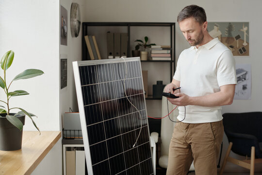 Engineer in smart casualwear using ammeter for testing power of solar panel while standing in office