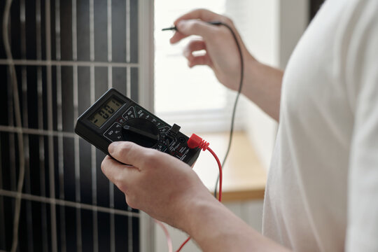 Hand of young male engineer or electrician with ammeter standing in front of solar panel before checking power