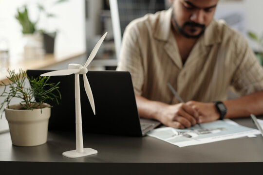 Windmill mockup and flowerpot with green plant standing by laptop against engineer drawing sketch