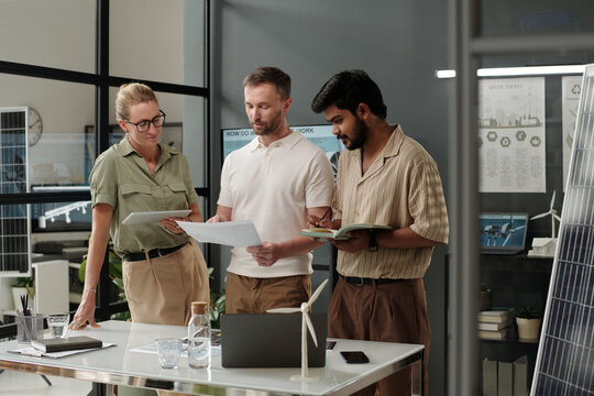Group of young intercultural architects preparing for presentation of new project while standing by workplace