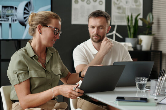 Businesswoman pointing at laptop screen while presenting online information to male colleague at meeting