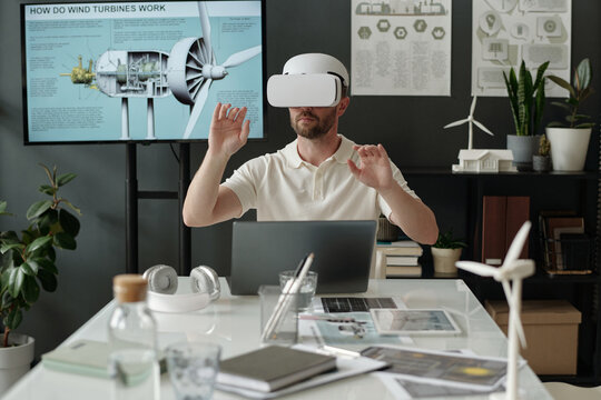 Young serious male architect with VR headset working with virtual presentation by workplace in office