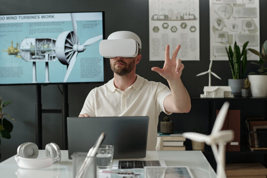 Modern businessman in VR goggle touching virtual screen while preparing presentation of new project