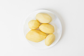 A white plate with five peeled potatoes, perfect for cooking holiday feasts or presenting vegetarian meal ingredients