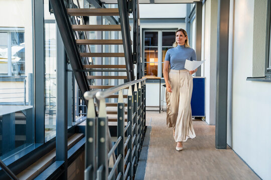Smiling businesswoman walking with documents in office corridor