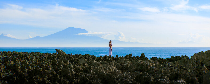 Woman standing on cliff near Nusa Dua ocean under cloudy sky