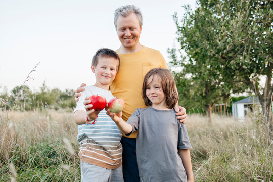 Father standing with sons holding apple at orchard - Powered by Adobe