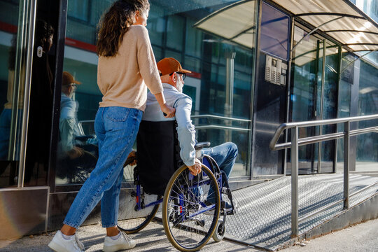 Caregiver pushing senior man in wheelchair on ramp