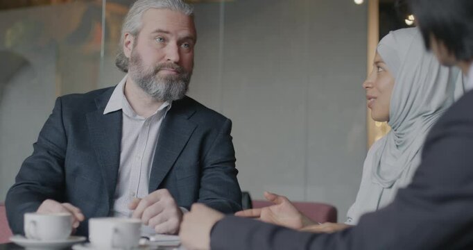 Middle Eastern woman in hijab interpreter translating business negotiations talking to men during meeting in cafe. Translation service and businesspeople concept.