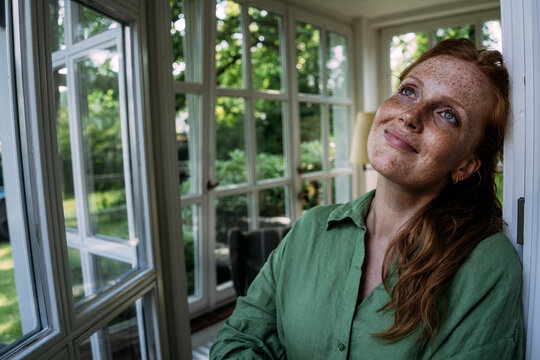 Thoughtful woman with freckles leaning on door