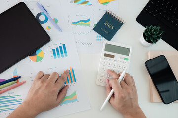 Business professional using calculator with financial charts at office desk