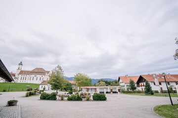 A quiet courtyard with a church, traditional houses, trees, and mountains in the background on a cloudy day..