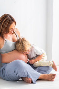 Pregnant mother spending leisure time with son near white wall
