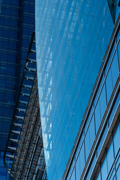 The image focuses on the facade of a skyscraper, highlighting the blue-tinted glass panels and modern architectural design with geometric patterns reflecting the sky.