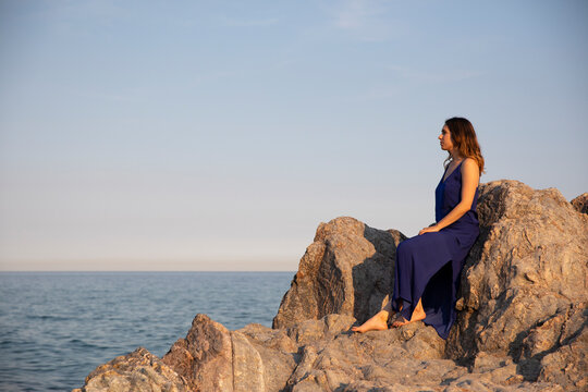 Thoughtful woman spending leisure time sitting on rock near sea