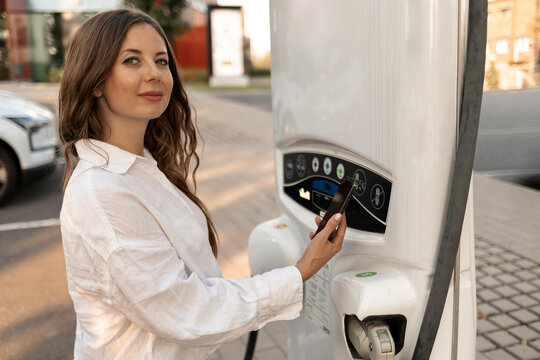 Woman paying through smart phone at car charging station