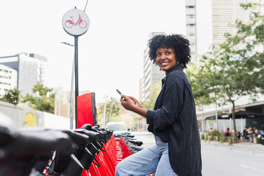 Smiling businesswoman holding smart phone sitting on electric bicycle
