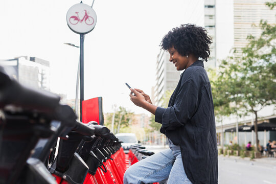 Afro businesswoman using smart phone sitting on electric bicycle