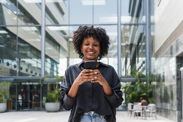 Smiling businesswoman using smart phone in front of office building
