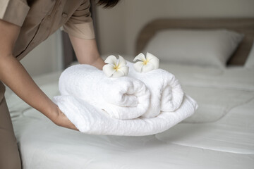 Hands of hotel maid putting plumeria flower and towels on the bed in the luxury hotel room ready for tourist travel