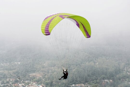 Paraglider flying high above village view and blue sky background