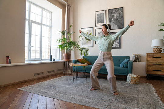 Happy woman wearing wireless headphones dancing at home
