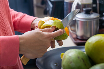 woman peeling ripe and juicy mango fruit with a sharp knife in the kitchen