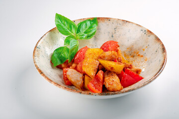 Vegetable ratatouille with potatoes, sweet peppers and tomatoes fried with garlic in a plate on a white background