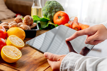 A woman is looking for a recipe on a tablet while preparing fresh vegetables on a wooden cutting board, healthy food concept