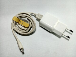 A still life composition of a plastic phone charger with a power socket and wire, showcasing technology, connection, and electricity concepts.