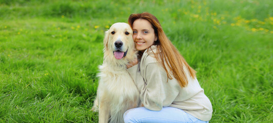 Happy owner young woman with Golden Retriever dog sitting on grass together in summer park